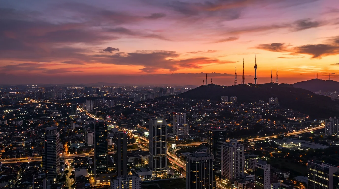 A wide photograph of a city skyline with distant broadcast towers at sunset.