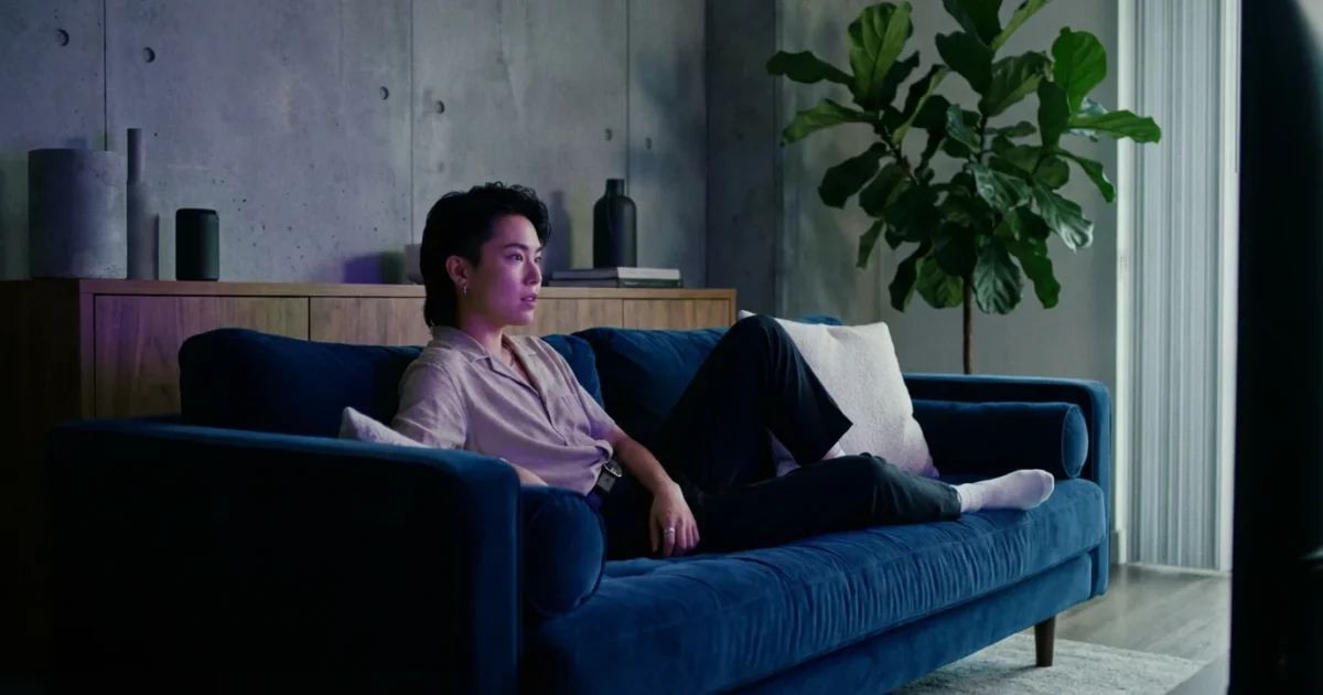 A person watching a movie in a cozy, modern living room with moody blue and purple lighting.
