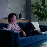 A person watching a movie in a cozy, modern living room with moody blue and purple lighting.