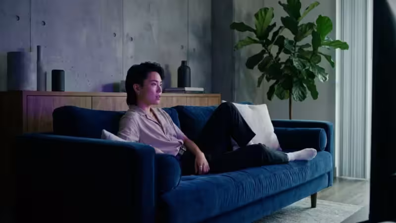 A person watching a movie in a cozy, modern living room with moody blue and purple lighting.