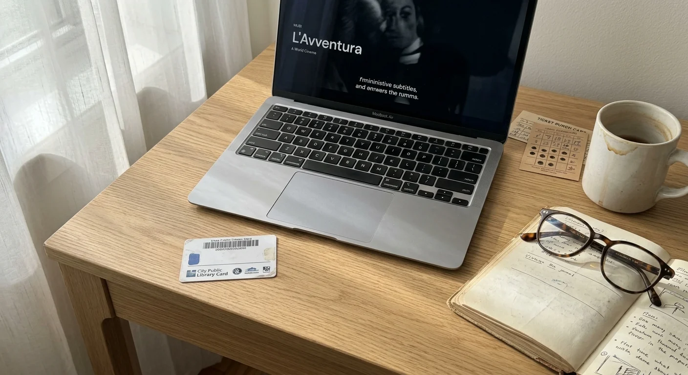 Laptop on a wooden desk next to a public library card, open notebook, eyeglasses, and a coffee mug.